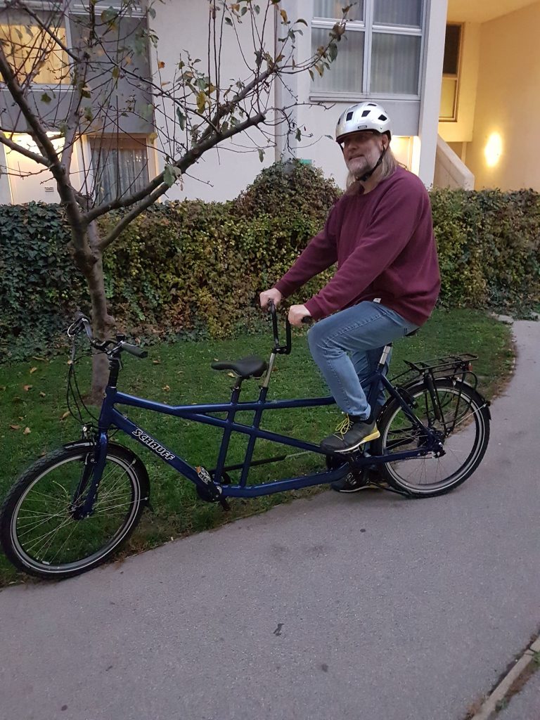 YetiFloridsdorf sitzt mit Hemd hinten auf einen Tandem-Fahrrad, das vor einem Haus steht