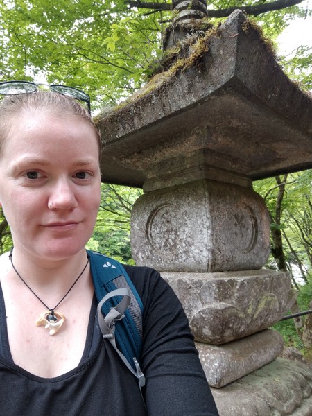 Selfie, draußen, Autistvsclichee steht vor einer Steinstatue und lächelt. 